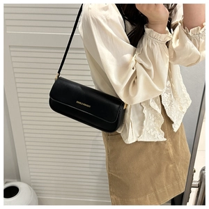 Détail d'un sac sous le bras en cuir noir minimaliste avec logo doré sur un mannequin