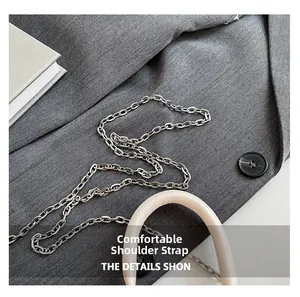 Detail of silver chain shoulder strap with cream leather handle on minimalist handbag