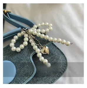 Detailed close-up of pearl bow charm with silver heart pendant on denim fabric background