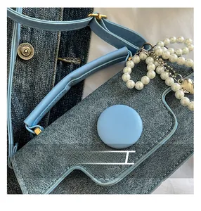 Detail of light blue denim mini bag with pearl chain handle and silver heart charm