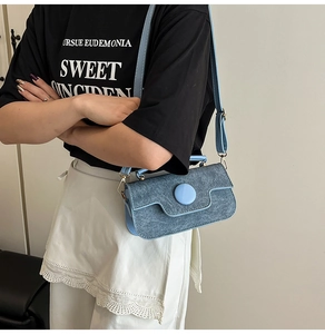 Detalle de bolso denim azul claro con hebilla redonda y correa de cuero ajustable