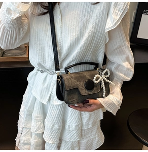 Detail of vintage grey crossbody bag featuring a large pearl bow charm on white lace dress