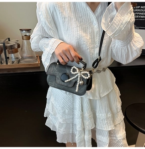 Detailed shot of dark grey square bag featuring pearl bow decoration and matte texture