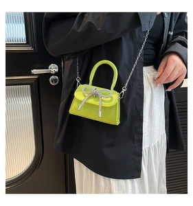 Close-up of neon green mini bag with rhinestone bow and silver chain on a white skirt