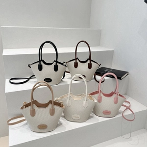 Minimalistische Eimer-Tasche mit Webstruktur in fünf Farben auf weißen Treppen