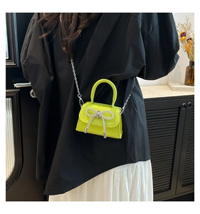 Detail of a bright green patent leather mini bag featuring a sparkling silver bow and chain