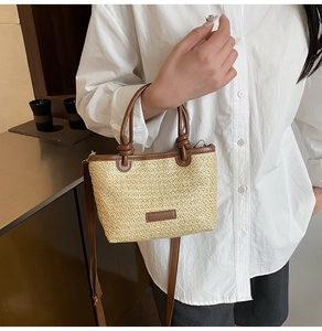 Détail du sac en paille tressée beige avec poignées en cuir marron et bandoulière longue