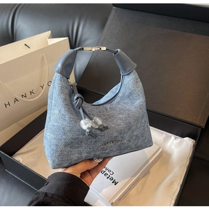 Detail of light blue denim crescent bag with metallic logo and luxury gift box packaging
