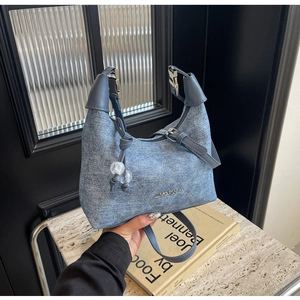 Close-up of light blue denim shoulder bag with quilted texture and metal plate