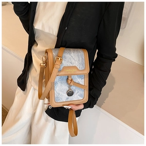 Detail of light blue denim and brown leather crossbody bag with a metal charm pendant