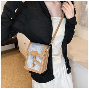 Detail of blue denim and brown leather crossbody bag with a gold metal pendant