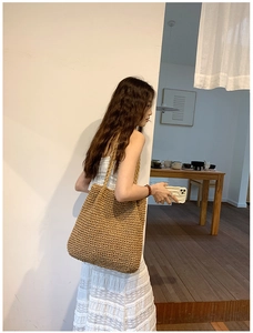 Detailed side view of a large khaki straw woven tote bag shown on a model