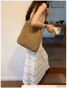 Detail of the large straw tote bag featuring woven texture and natural brown shoulder straps