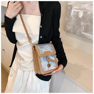 Detail showing vintage denim crossbody bag with brown leather trim and metal charm