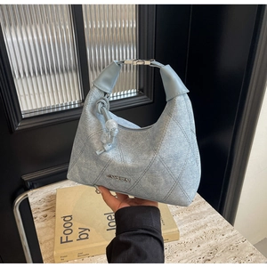 Detail of light blue denim quilted hobo bag with JINGPIN logo and ball charm on marble
