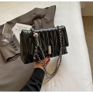 Détail du sac matelassé noir avec chaîne argentée et pendentif boule métallique