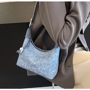 Detail of blue denim crescent bag featuring metal logo and beaded knot strap detail