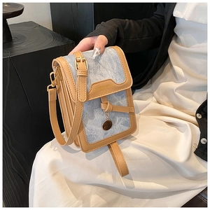 Detail showing blue denim and brown leather patchwork bag with gold metal pendant