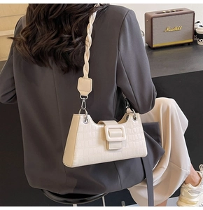 Detail of white crocodile embossed baguette bag featuring woven strap and metal buckle