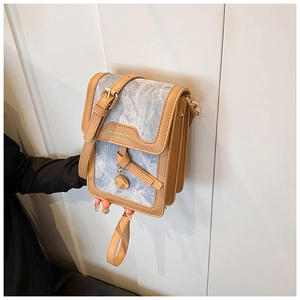 Detail of light blue denim crossbody bag with brown leather trim and metal charm