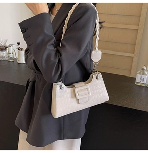Detail of white crocodile embossed baguette bag featuring a braided shoulder strap design