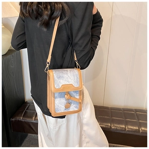 Detail of light blue denim fabric crossbody bag with brown leather trim and gold charm