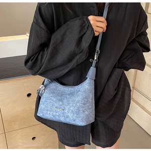 Detail view of denim blue hobo bag with vintage texture and metal logo plaque