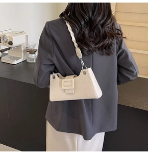 Detail of cream baguette bag with crocodile texture and woven shoulder strap