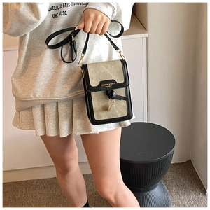 Detailed shot of beige canvas and black leather crossbody phone bag with leaf charm
