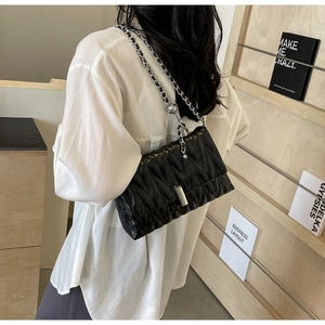 Détail d'un sac bandoulière matelassé noir avec chaîne argentée sur le mannequin