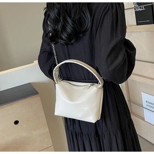 Detail of white glossy shoulder bag with silver chain strap worn by a woman in black dress