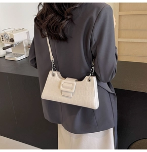 Detail of cream baguette bag with crocodile texture and large decorative buckle