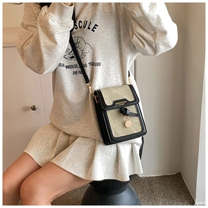 Detail of a small black and beige crossbody phone bag with gold charm and fashion lettering