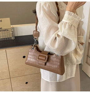 Close-up of brown crocodile texture baguette bag with braided shoulder strap and buckle