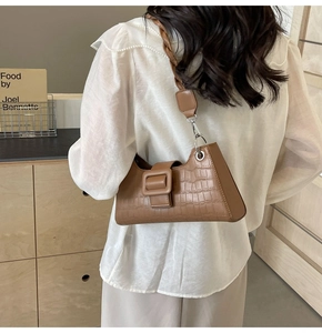 Chic tan baguette bag with croc pattern and woven strap on model in minimalist interior
