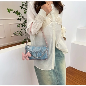 Detail view of light blue denim shoulder bag with pink puppy charm and metal chain strap