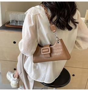 Close-up of brown crocodile texture shoulder bag with large square buckle and twisted strap
