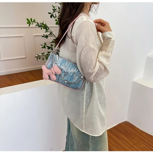 Detail of light blue textured shoulder bag with pink puppy pendant and metal chain accessory