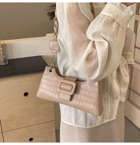 Close-up detail of beige crocodile embossed leather and square buckle on baguette bag