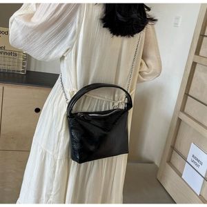 Detail of black glossy bucket bag with silver chain strap and wrinkled leather texture