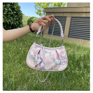 Detailed embroidery of floral patterns on a pale pink crossbody bag with silver chain