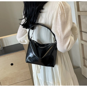 Detail of black patent leather bucket bag with silver chain strap on white dress