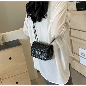 Détail d'un sac matelassé noir avec bandoulière en chaîne et fermoir métallique