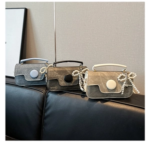 Detailed view of color-block flap bags in grey tones with pearl bow charms on leather sofa