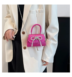 Detail of rose pink sequin mini bag with rhinestone bow and metal chain strap on model