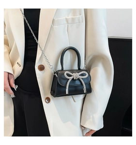Close-up of black mini bag with oversized silver rhinestone bow and chain strap