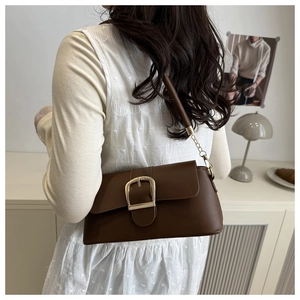 Deep brown leather underarm bag with a large gold metal buckle shown on a model