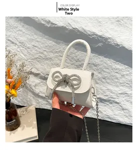 Detail of white mini bag with sparkling rhinestone bow and silver metal chain strap