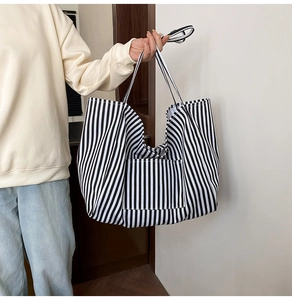 Close-up of black and white striped canvas tote bag with front pocket held by model