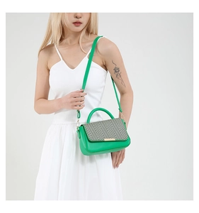 Sac bandoulière vert avec rabat tissé et détails dorés porté sur une robe blanche
